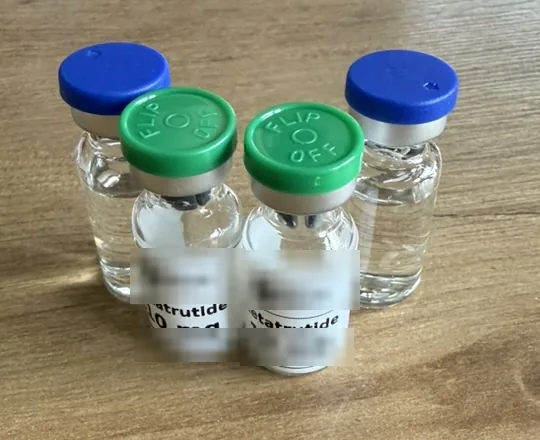 Zwei Vials Retatrutid und zwei Vials bakteriostatisches Wasser auf einem Holztisch